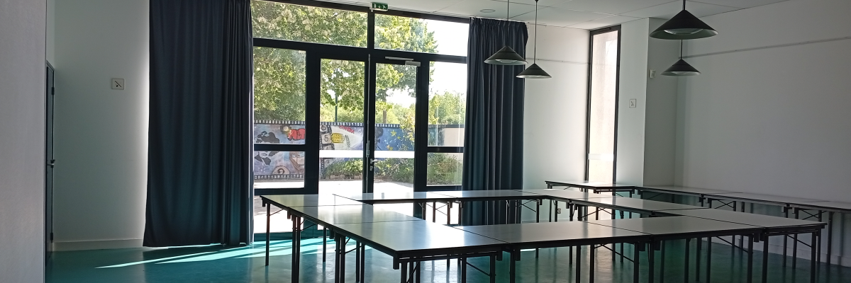 Salle avec tables, chaises, luminaires suspendus et grandes fenêtres.