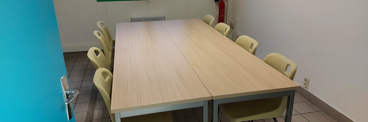 Salle avec table rectangulaire, chaises, fenêtre, extincteur et climatiseur.