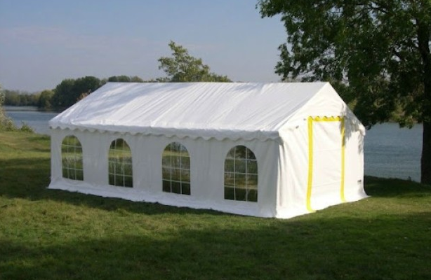 Tente blanche avec fenêtres sur un terrain herbeux près d'un plan d'eau.