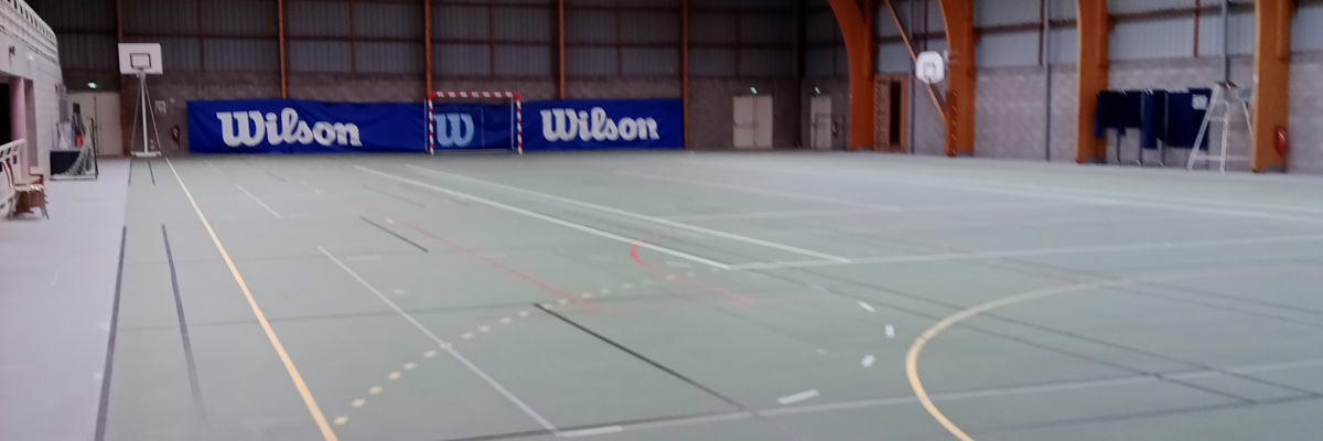 Terrain de sport intérieur avec lignes de tennis et de basket.