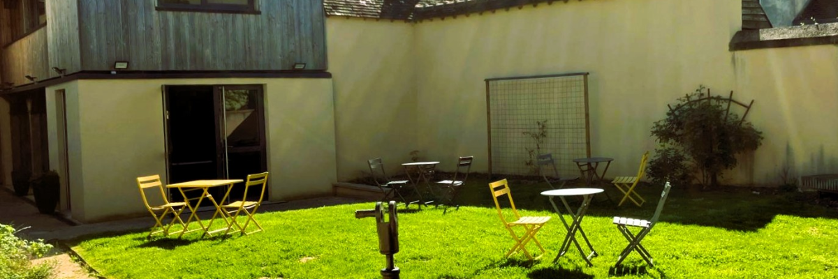 Cour avec tables, chaises, robinet et bâtiments en arrière-plan.