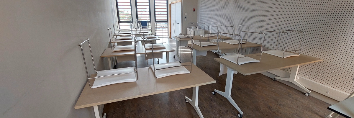 Salle de classe avec bureaux, chaises et tableau blanc.