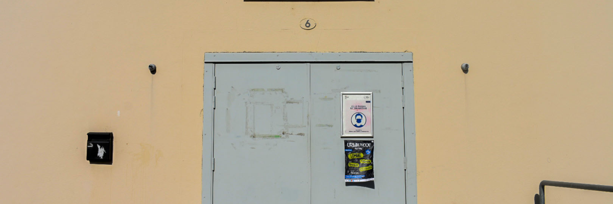 "Porte métallique bleue avec enseigne 'Salle Polyvalente', boite aux lettres, affiches et rampe d'accès."