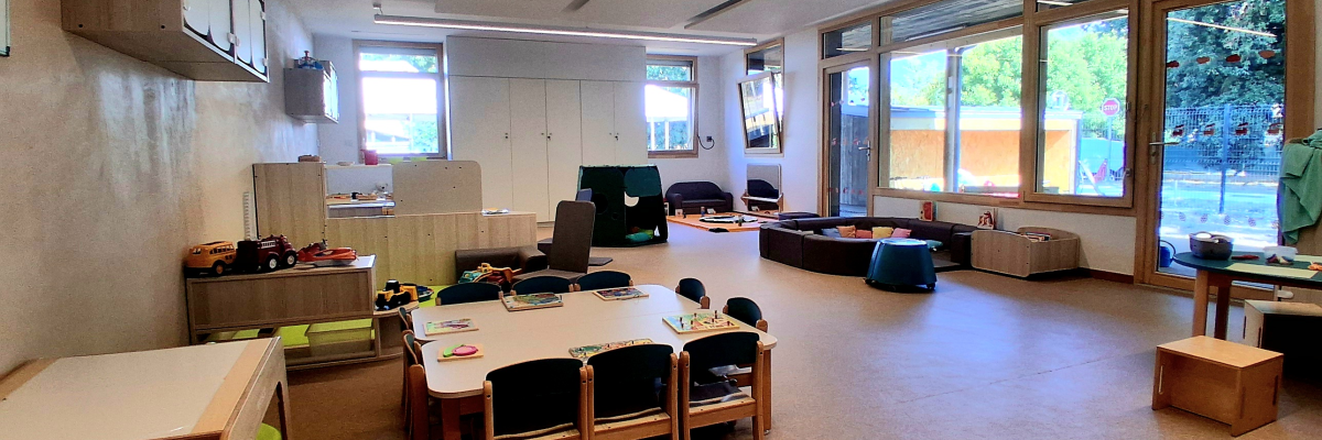 Salle avec tables, chaises, coussins, étagères, télévision, luminaires, fenêtres, porte-manteau.