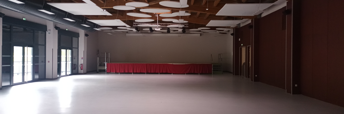 Grande salle avec plafonniers ronds, grandes fenêtres, porte et rideau rouge.