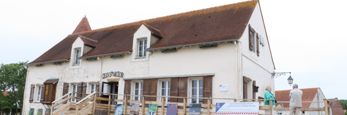 Bâtiment avec toit en pente, portes en bois, fenêtres, panneau d'affichage et clôture.