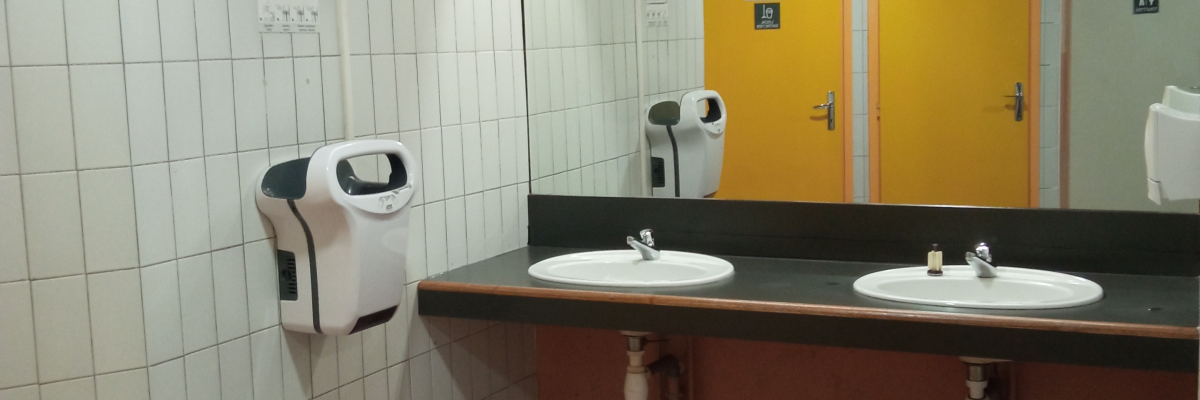 Toilettes avec lavabos, sèche-mains, distributeur de savon et sol carrelé.