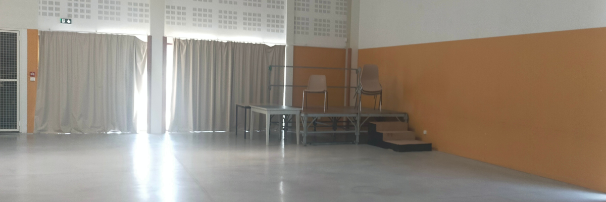 Salle avec rideaux, table, chaises, escaliers et projecteur.