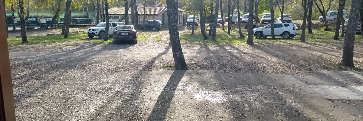 Parking avec voitures, arbres et bâtiment en arrière-plan.