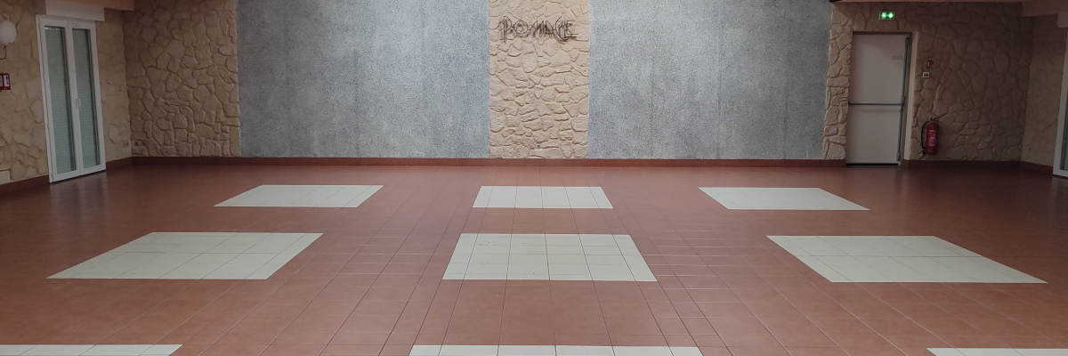 Salle vide avec sol carrelé rouge et blanc, murs en pierre et faux plafond.