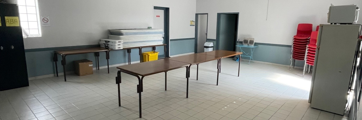 Pièce avec tables, chaises, armoires, étagère, climatiseur, frigo, et porte.