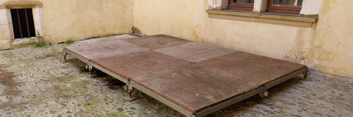 Table en bois sur sol pavé devant un mur avec fenêtres.