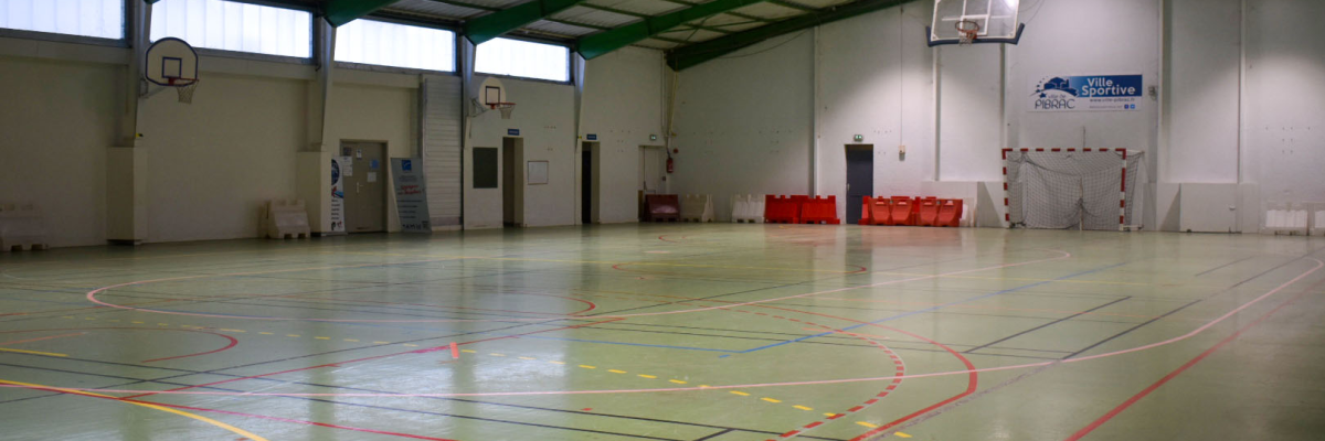 Gymnase avec paniers de basket, terrain de handball et portes orange de sécurité.