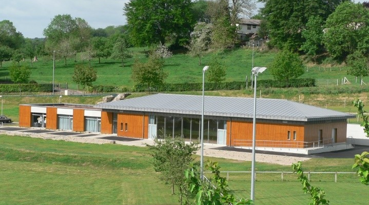 Bâtiment orange avec toit gris, situé dans un environnement vert et arboré.