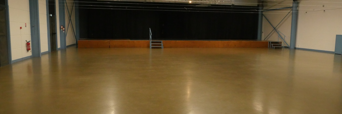 Grand espace avec sol en béton, murs blancs, éclairage LED, écran noir, escaliers.