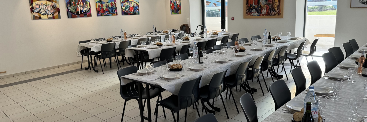 Salle de repas avec tables, chaises, verres, assiettes, couverts et bouteilles.