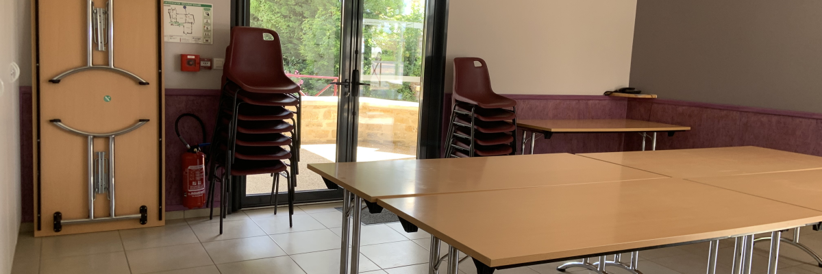Salle avec tables, chaises empilées, porte et armoire à portes métalliques.