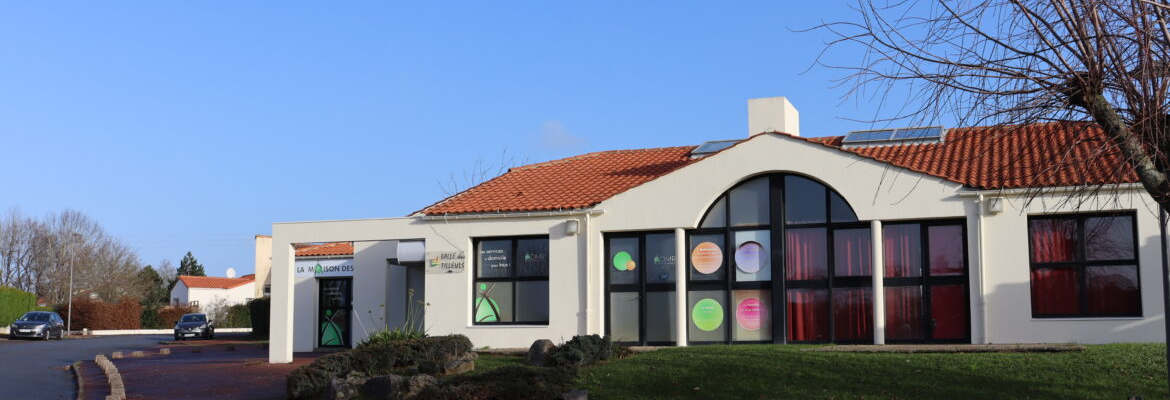 Bâtiment blanc avec toiture rouge, grandes fenêtres, parking et végétation.
