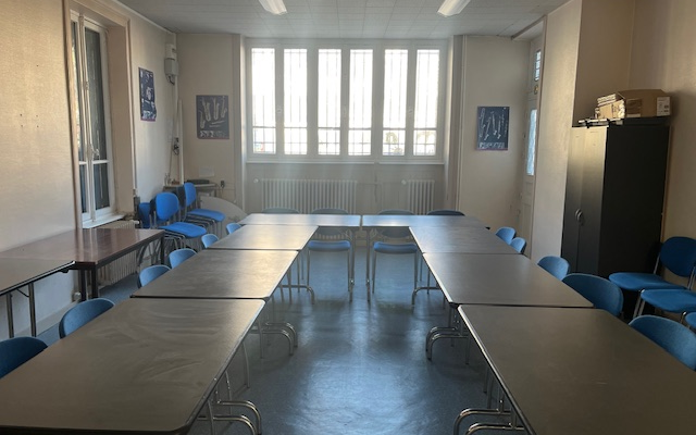 Salle avec tables, chaises, fenêtres et radiateurs.