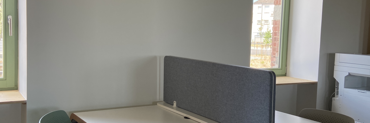 Bureau avec séparateurs, deux chaises vertes et tabouret circulaire.