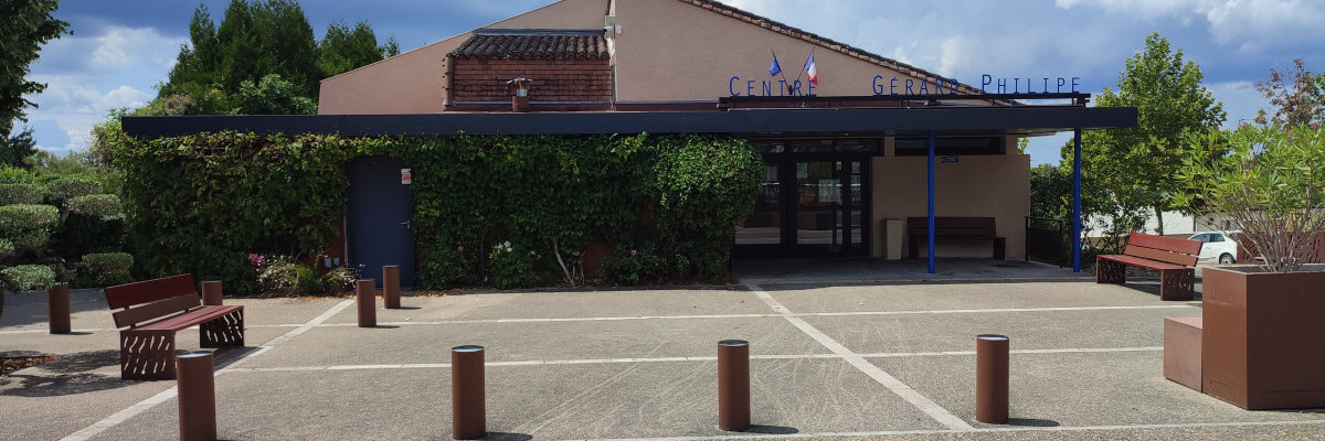 Bâtiment avec enseigne, parking, bacs à fleurs, bancs.