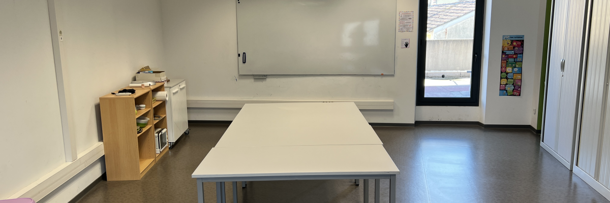 Salle avec table, chaises, tableau, étagères, vidéoprojecteur et climatiseur.