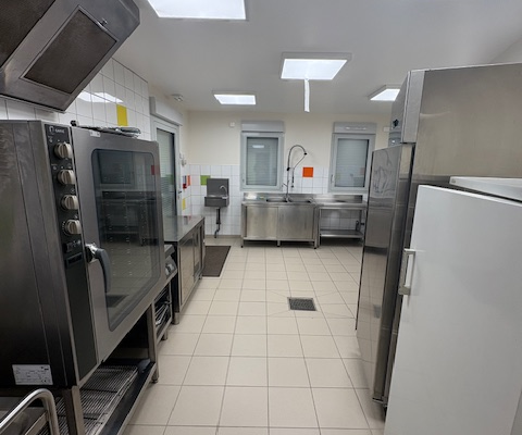 Cuisine avec fours, évier, réfrigérateurs, sols carrelés et éclairage encastré.