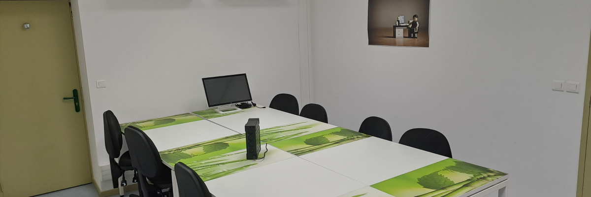Salle de réunion avec table, chaises, ordinateur, étagères et cadre photo.