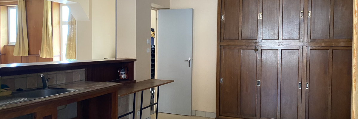 Cuisine avec comptoir, évier, placards en bois, tabourets, porte et miroir.