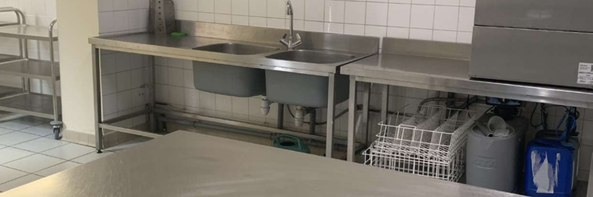 Cuisine avec plans de travail, évier, lave-vaisselle, étagères et paniers.