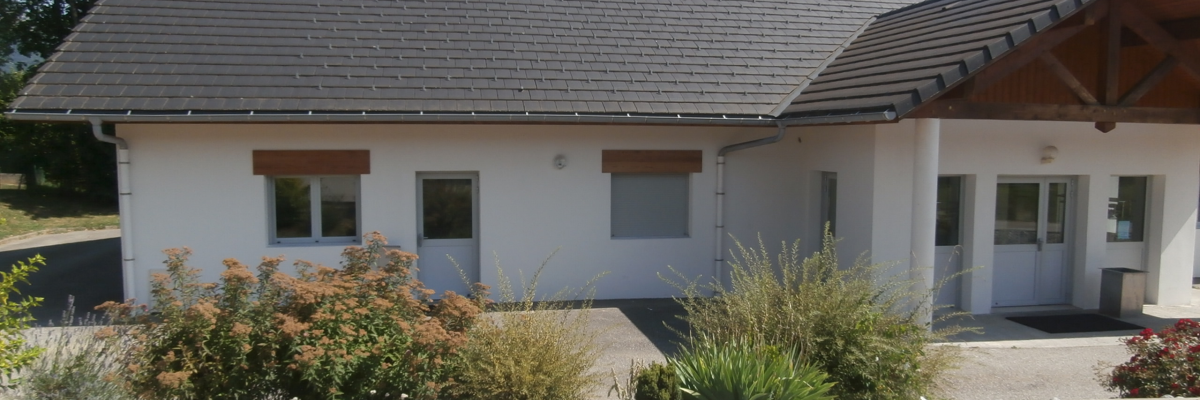 "Bâtiment à toit pentu, portes et fenêtres blanches, plantes et allée."