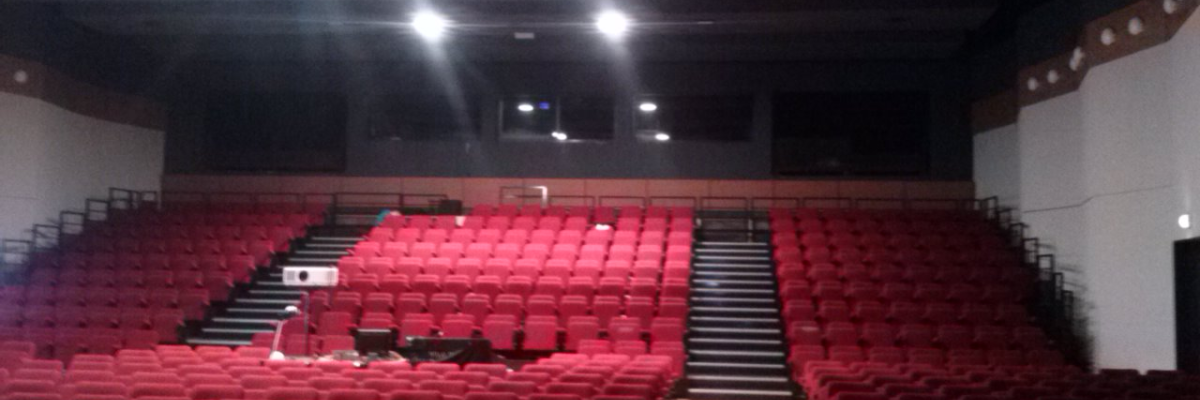 Salle de spectacle avec sièges rouges, scène et écran.
