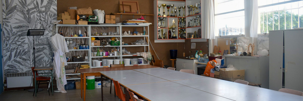 Salle avec étagères, table, chaises, matériel pédagogique, fenêtre et équipements de classe.