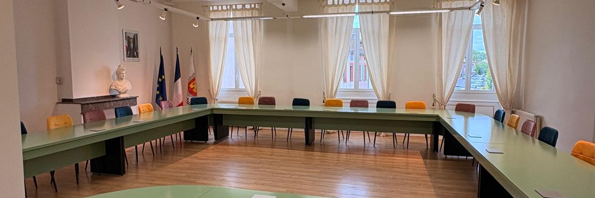 Salle de réunion avec table, chaises, projecteur et écran.