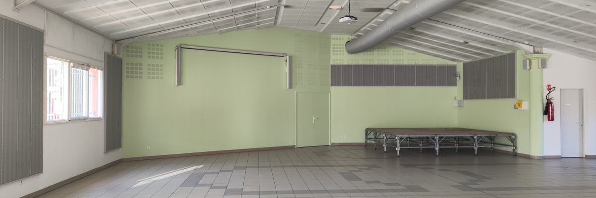 Salle vide avec bancs, extincteurs, ventilations au plafond et murs verts.