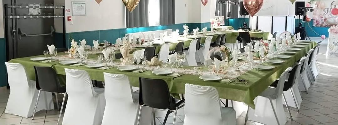 Salle avec tables, chaises, nappes, verres, couverts, ballons en forme de coeur.