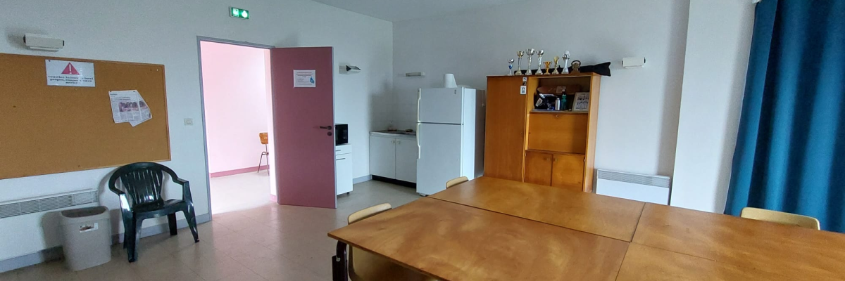 Salle avec table, chaises, armoire, frigo, tablette, tableau d'affichage et porte.