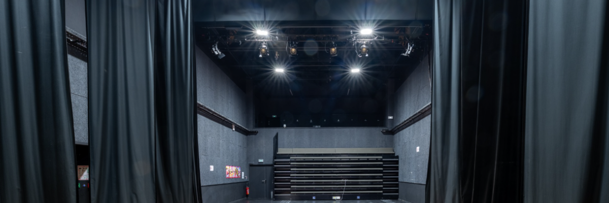 Salle avec éclairages, gradins, rideaux et tapis rouge.
