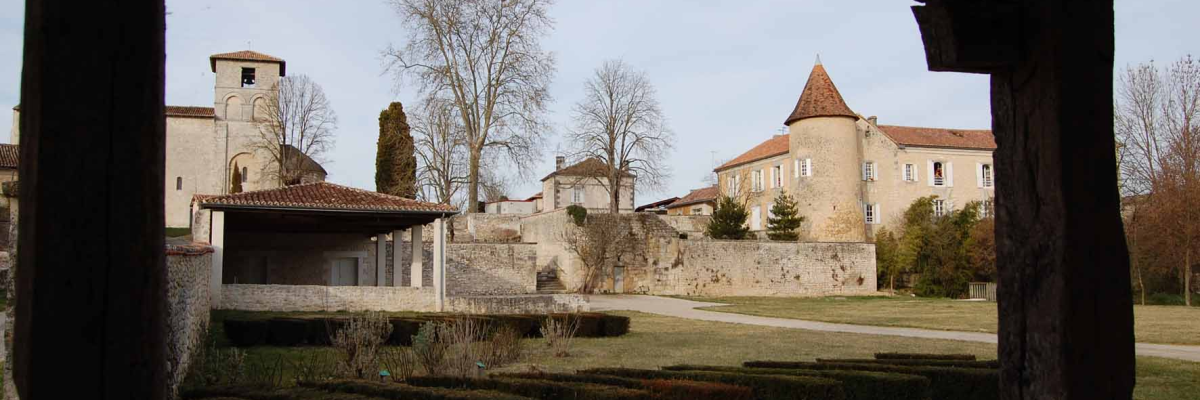 Vue d'une cour avec bâtiments anciens, arbres et buissons.
