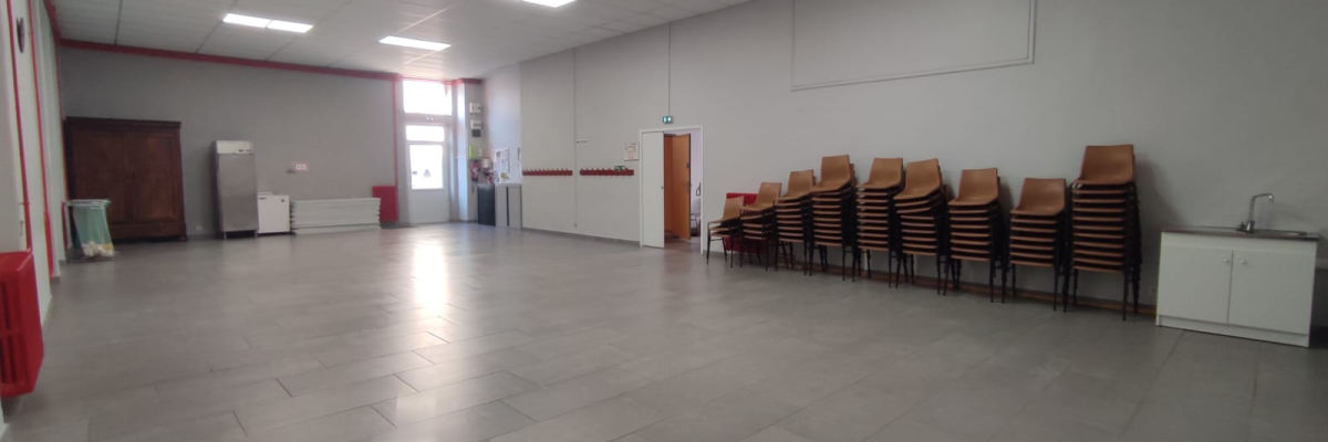 Salle vide avec chaises empilées, évier et meuble de rangement.