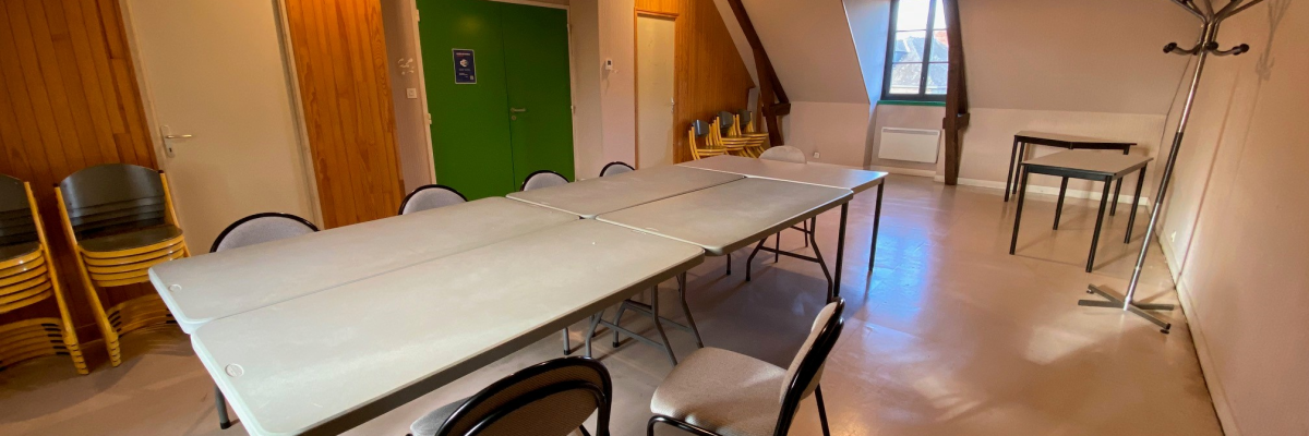 Salle avec table, chaises, porte-manteau, porte verte, fenêtres.