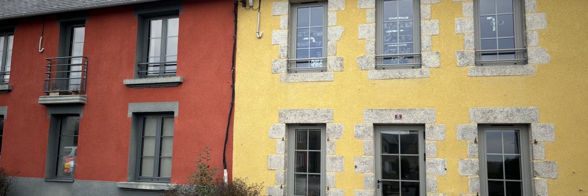 Maison mitoyenne, deux couleurs (rouge et jaune), toit en ardoise, fenêtres avec volets, porte d'entrée.