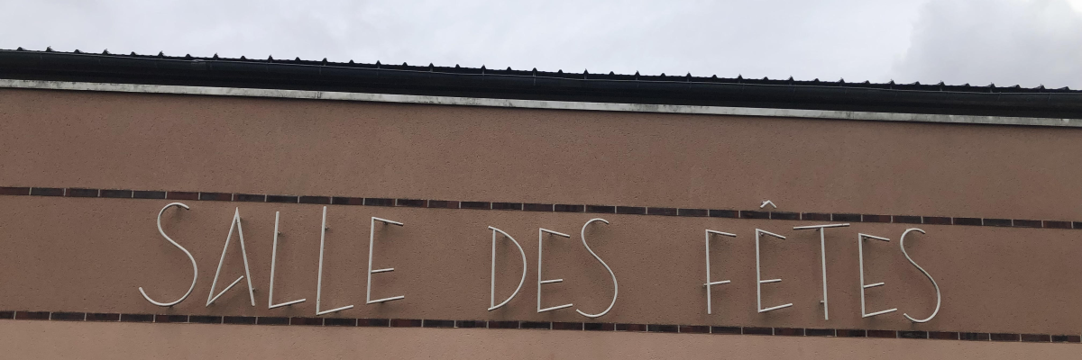 "Salle des fêtes" écrit en néon sur un mur beige.