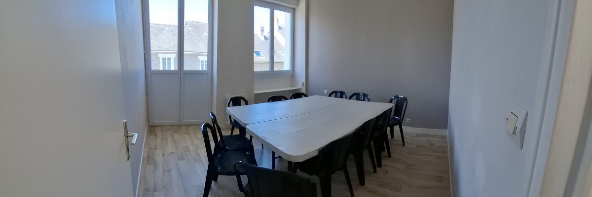 Salle avec table, chaises, portes vitrées et parquet.