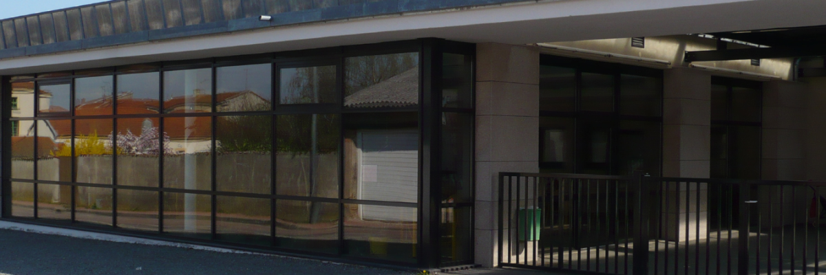 Bâtiment avec grandes baies vitrées reflétant des structures avoisinantes, escalier à droite.