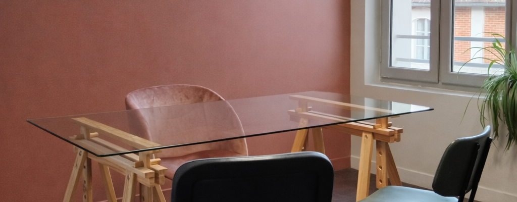 "Pièce avec table en verre, chaises, étagères, plante, fenêtre et cadre mural."