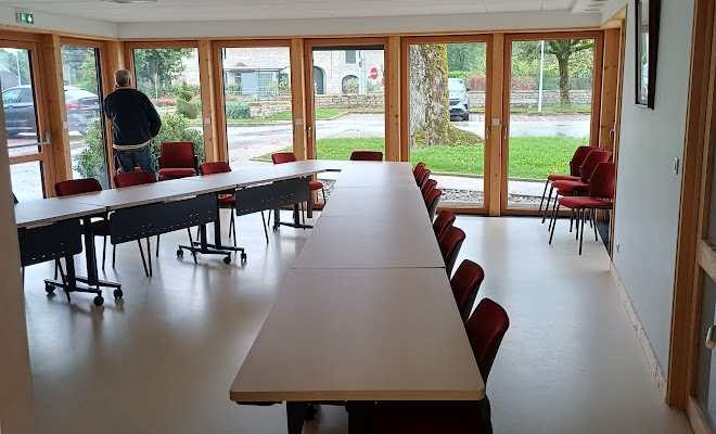 Salle avec tables, chaises, vidéo projecteur, portes vitrées.