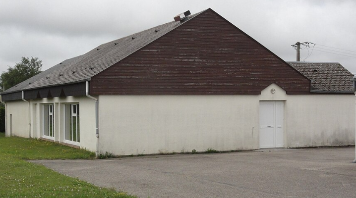 Bâtiment avec toit en pente, murs blancs, fenêtres et porte.