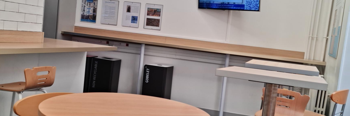 Espace avec tables, chaises, comptoir, écran, affiches.