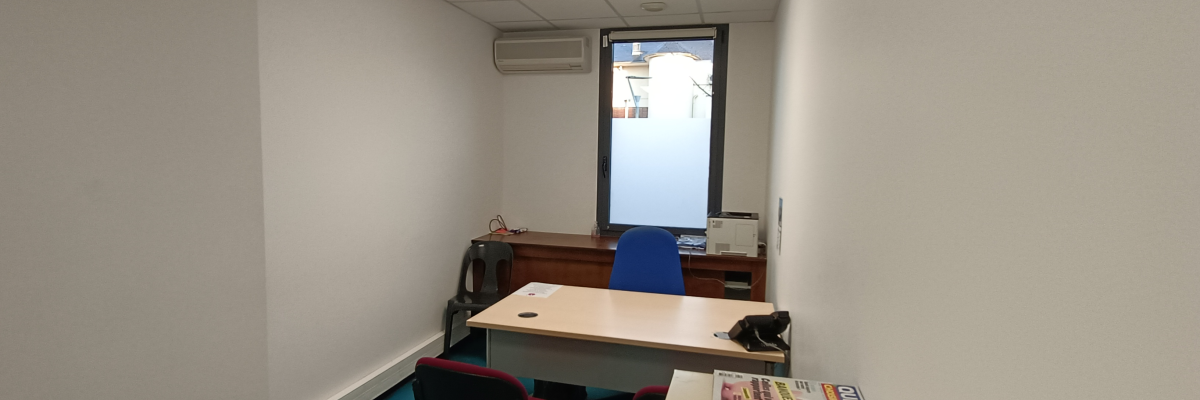 Bureau avec table, chaises, climatiseur, bouilloire, imprimante et documents.
